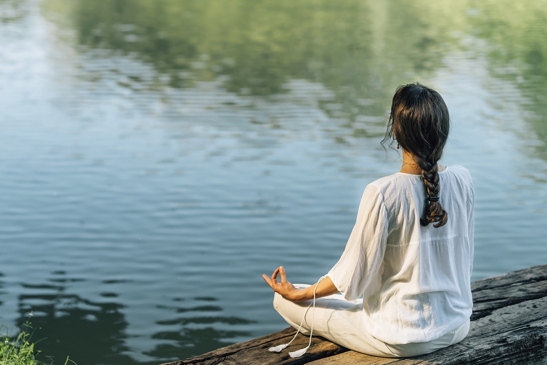 Yoga Retreat. Peaceful young woman sitting in lotus position and meditating by the lake